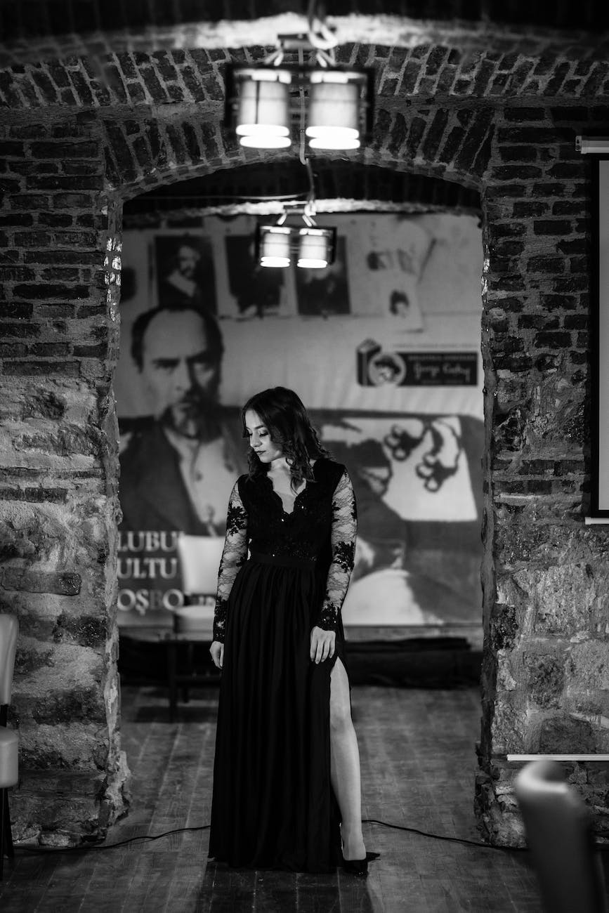 grayscale photography of woman under pendant lamp